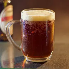 Chłodne piwo w kuflu, idealna temperatura piwa na upalny dzień. W tle butelka piwa.