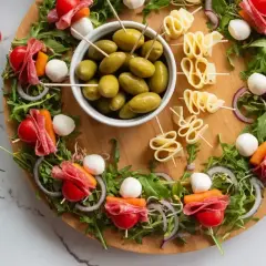 Kolorowa deska z przekąskami: szaszłyki z pomidorkami, mozzarellą, salami i marchewką, oliwki, ser do sałatek.