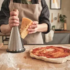 Ręce trzymają kawałek sera i tarkę, przygotowując się do starcia go na pizzę. To idealny sposób, czym posmarować pizzę, by była pyszna!