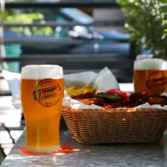 Orzeźwiające piwo białe z pianką, obok koszyk z przekąskami i kolejny kufel. Idealne na letni wieczór.