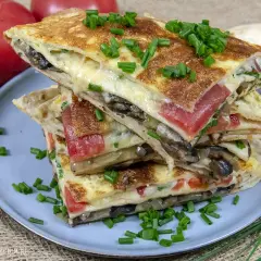 Pyszna tortilla na śniadanie z serem, pomidorami i grzybami, posypana szczypiorkiem.