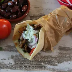 Pyszny pita gyros z soczystym mięsem, warzywami i kremowym sosem, obok pomidory, oliwki i cebula.
