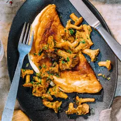 Złocisty omlet z kurkami, posypany natką pietruszki, czeka na widelcu. Pyszne danie na śniadanie lub lekki obiad.