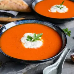 Aksamitny zupa krem z papryki, udekorowana śmietaną i natką pietruszki, podana z pieczywem i czosnkiem.