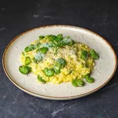 Risotto z bobem i parmezanem, jedno z pysznych włoskich dań głównych, udekorowane gałązką rozmarynu.