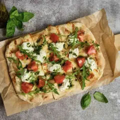 Pyszna pizza wege z pomidorami, mozzarellą i rukolą, polana zielonym pesto. Idealna na lekki posiłek.