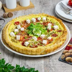 Tarta z pomidorami i kostkami sera mozzarella starta, ozdobiona kiełkami i ziołami.