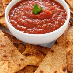 Chrupiące nachos otaczają miseczkę z aromatyczną, domową **salsą pomidorową**, ozdobioną listkiem pietruszki. Idealna przekąska!