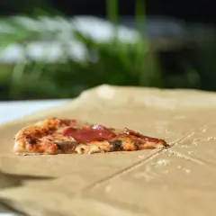 Kawałek pizzy z salami na śniadanie, leżący na papierze do pieczenia.