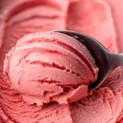 Pyszne, domowe lody truskawkowe z przepisu. Łyżka nabiera porcję kremowego, różowego deseru.