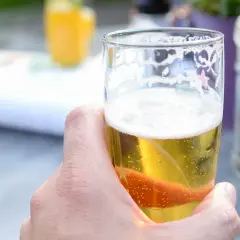 Dłoń trzymająca szklankę orzeźwiającego piwa dietetycznego. W tle widać pomarańczowy napój i młynki do przypraw.