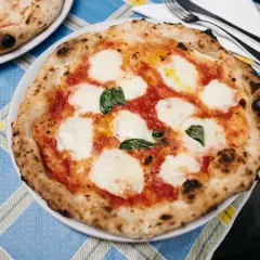 Pyszna pizza z samym serem, pomidorami i bazylią, z chrupiącym, lekko przypalonym brzegiem, na niebiesko-żółtym obrusie.