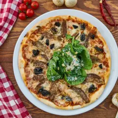 Idealna pizza z piwem na drewnianym stole, ozdobiona rukolą i parmezanem. Obok czosnek, pomidorki i rozmaryn.