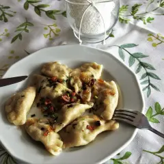 Pyszne pierogi Ania gotuje, polane skwarkami i szczypiorkiem. Na talerzu obok widelca i noża.