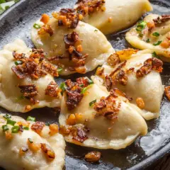 Pyszne pierogi z mięsem mielonym, okraszone skwarkami i szczypiorkiem, podane na żeliwnej patelni.
