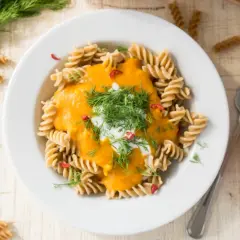 Makaron fusilli z kremowym sosem z **hokkaido dyni**, udekorowany koperkiem i chili. Obok talerza leży cała dynia.