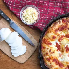 Idealny jaki ser do pizzy? Na desce świeża mozzarella, obok nóż i miseczka z tartym serem. Obok pyszna, gorąca pizza.