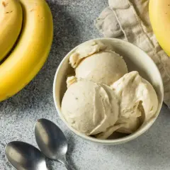 Pyszne lody bananowe w miseczce, obok świeże banany i łyżeczki. Idealne na upalny dzień.