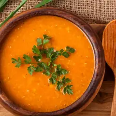 Aksamitna zupa pomidorowa w drewnianej misce, udekorowana natką pietruszki. Obok łyżka i kromki chleba.