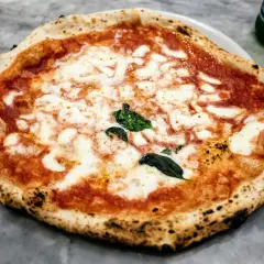 Nietypowa pizza margherita z lekko przypalonymi brzegami i świeżą bazylią, prezentująca się apetycznie na marmurowym blacie.