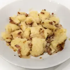 Pyszne, domowe szare kluski z boczkiem i cebulką, podane w białej miseczce. Idealne na obiad!