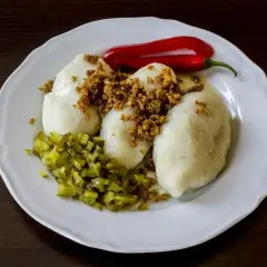 Gotowe kartacze na talerzu, posypane skwarkami, z ogórkiem kiszonym i papryczką chili. Idealne do podania według przepisu na kartacze.