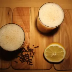 Dwa szklanki piwa z jajkiem, obok cytryna i goździki na drewnianej desce.