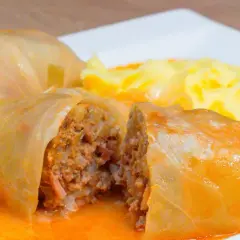 Pyszne gołąbki w sosie pomidorowym, jeden przekrojony, ukazujący farsz z mięsa i ryżu. Obok puree ziemniaczane.