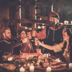 Ludzie w strojach z epoki wznoszą toasty przy suto zastawionym stole. To scena z historii piwa, gdzie napój ten towarzyszył ucztom od wieków.