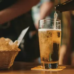 Złociste piwo IPA i APA leje się do szklanki. Obok koszyk z przekąskami.