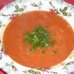 Aromatyczna zupa pomidorowa na bulionie warzywnym, udekorowana świeżą natką pietruszki, podana w ozdobnej porcelanowej misce.