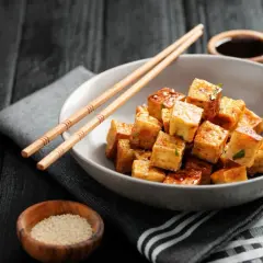 Kostki smażonego tofu, z którego jest tofu, w sosie, pałeczki, sezam i sos sojowy na ciemnym tle.