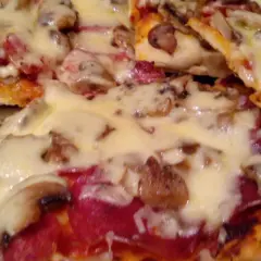 Pyszna domowa pizza z pieczarkami i salami, obficie posypana ciągnącym się serem. Idealna na wieczór z bliskimi.