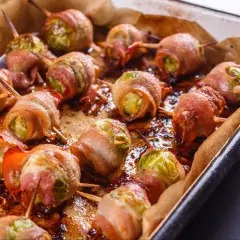 Pyszna, pieczona brukselka zawinięta w chrupiący boczek, ułożona na blasze wyłożonej papierem do pieczenia.