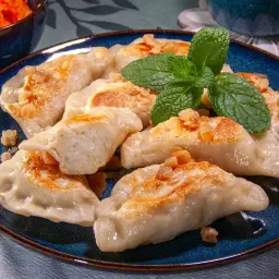 Gotowe pierogi z mięsem, posypane skwarkami i udekorowane miętą. Idealny przepis na obiad.