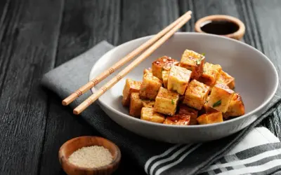Kostki smażonego tofu, z którego jest tofu, w sosie, pałeczki, sezam i sos sojowy na ciemnym tle.