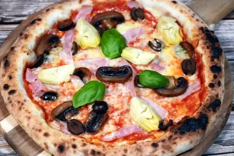 Pizza Capriciosa z klasycznymi składnikami: szynką, pieczarkami, karczochami i oliwkami.