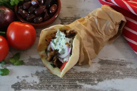 Pyszny pita gyros z soczystym mięsem, warzywami i kremowym sosem, obok pomidory, oliwki i cebula.