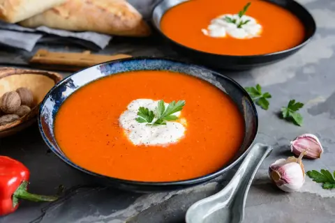 Aksamitny zupa krem z papryki, udekorowana śmietaną i natką pietruszki, podana z pieczywem i czosnkiem.