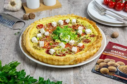 Tarta z pomidorami i kostkami sera mozzarella starta, ozdobiona kiełkami i ziołami.