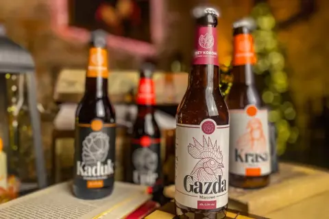 Piwo z Pomorza: butelki "Kaduk", "Gazda" i "Krasa" stoją na stole obok otwartej książki i szachownicy.