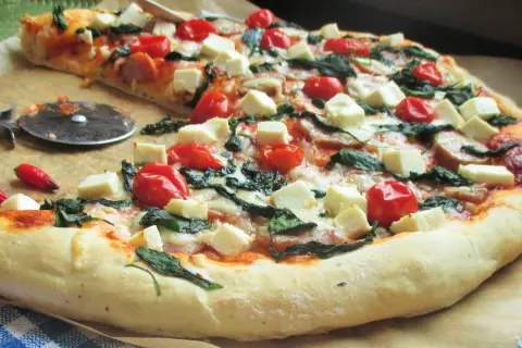 Pyszna pizza z fetą, pomidorkami koktajlowymi i szpinakiem, gotowa do pokrojenia.
