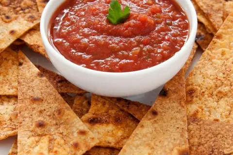Chrupiące nachos otaczają miseczkę z aromatyczną, domową **salsą pomidorową**, ozdobioną listkiem pietruszki. Idealna przekąska!