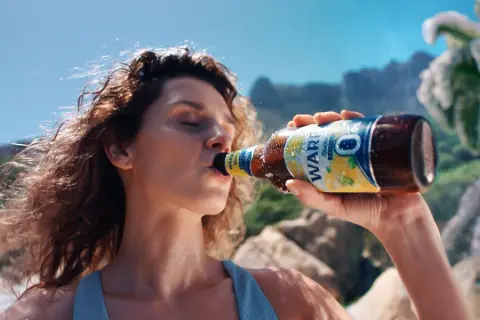 Kobieta pije piwo Zlatý Bažant 0,0% na plaży.