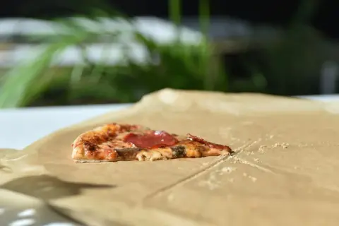 Kawałek pizzy z salami na śniadanie, leżący na papierze do pieczenia.