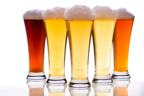 Pięć kielichów z piwem, w tym ciemny bursztynowy i jasny pilsner, z obfitą pianką.