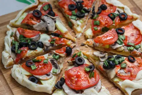 Kawałki pysznej, **zdrowej pizzy** z pomidorami, oliwkami i pieczarkami na drewnianej desce.