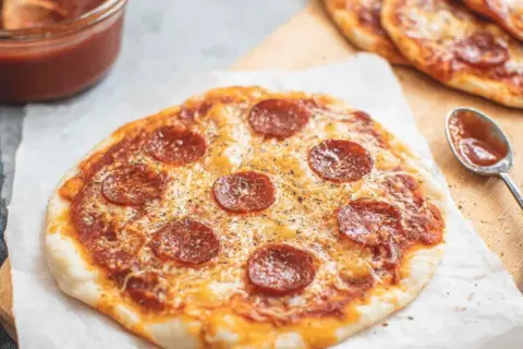 Pyszna pizza z tortilli z pepperoni i serem, obok sos i łyżeczka.