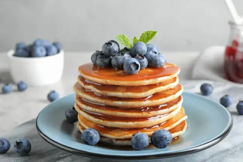 Pyszne, złociste pancake amerykańskie polane syropem i ozdobione świeżymi borówkami.
