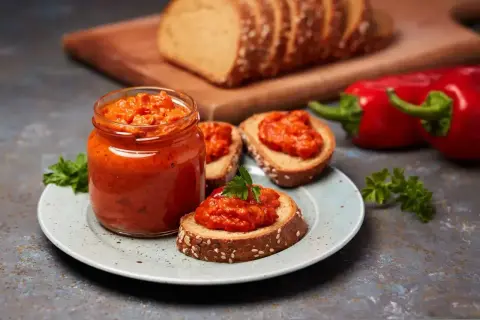 Słoik pełen pysznego sosu paprykowego, podany z chlebem i świeżymi paprykami. Idealny na przekąskę!